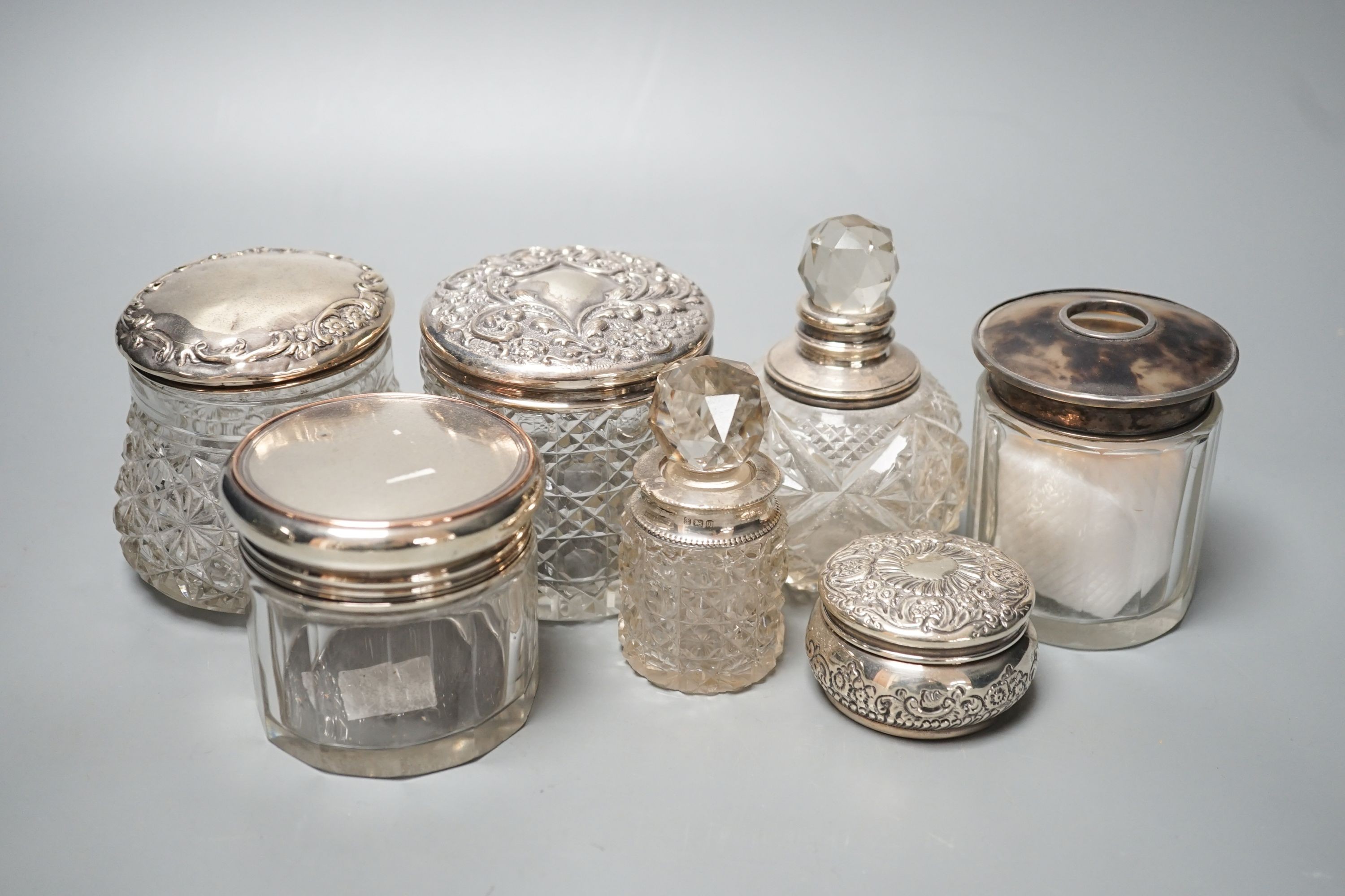 A circular embossed silver box and six silver mounted glass toilet bottles.